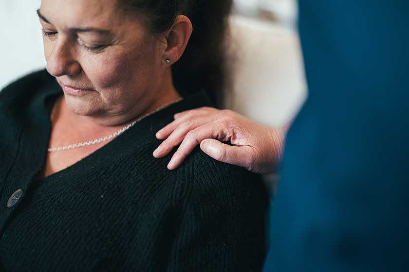 A caregiver rests their hand on a woman's shoulder